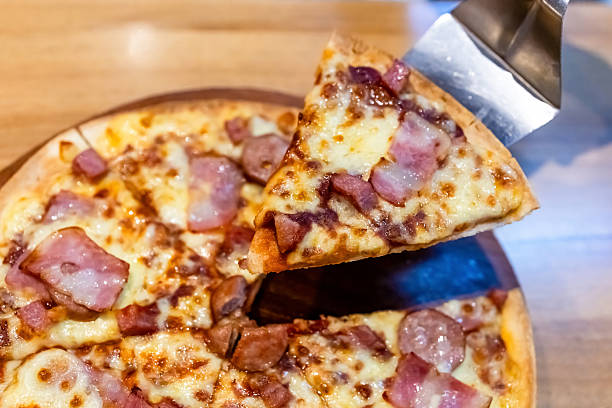 Slice of bacon and cheese pizza being lifted from the tray. Melted cheese and crispy bacon topping creating a delicious fast food and restaurant meal scene