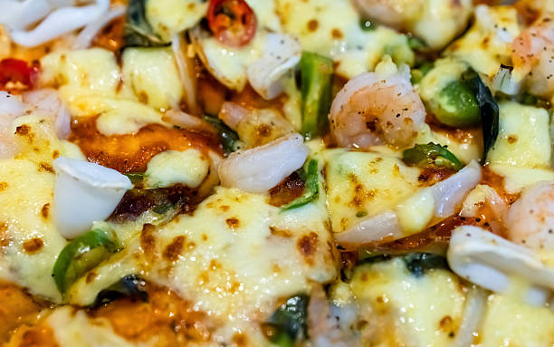 Seafood pizza with shrimp, squid, vegetables and melted cheese, close-up. Rich textures and colorful toppings create an appetizing gourmet fast food background