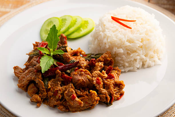 Close up Stir fried sliced Beef with dry chilli and Holy Basil and cooked thai rice in white plate.