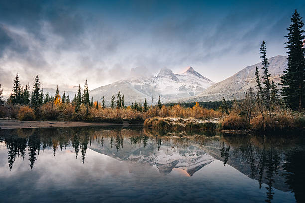Scenic view of the Three Sisters mountain peaks rising above colorful autumn forest in Canmore, Alberta, Canada, within the Canadian Rockies.