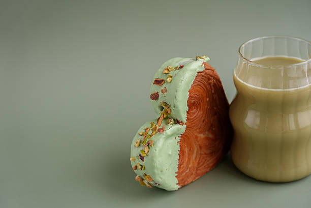 Green tea Matcha latte cappuccino beverage Morning breakfast gift idea Heart shaped pistachio croissant on green background with copy space. Puff pastry trendy sweet dessert bakery. Creamy dough experiment