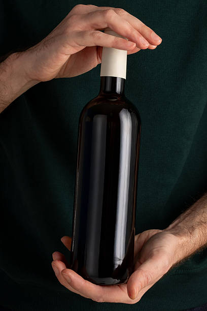 Man hands holding dark wine bottle blank white label dark green background elegant indoor presentation