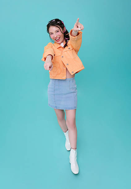Asian woman pointing at camera and smiling in studio expressing engagement confidence interactive communication call to action and energetic modern lifestyle concept