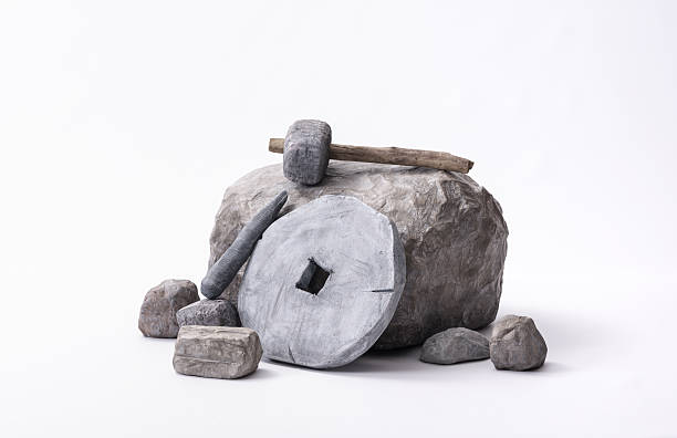 A stone chisel, a stone wheel, and a stone hammer resting on a rock, photographed on a white background to represent construction and conceptual ideas