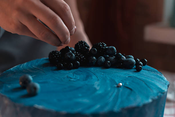 Adding fresh berries on blue frosted cake close up