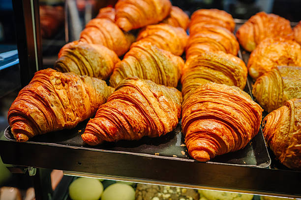 Freshly baked golden croissants arranged neatly on a display shelf in a bakery, showcasing flaky layers and appetizing texture under warm lighting
