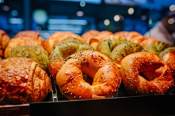 Freshly baked assorted bagels with sesame and poppy seeds displayed in a bakery, showcasing a variety of colors and textures under warm lighting