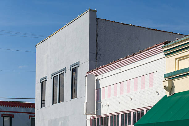 A view of historic commercial buildings along the main street in downtown Brenham, Texas. The architecture features early 20th century storefronts with painted brick facades in white, pink, and green colors. The buildings display typical small-town commercial design with large windows and decorative cornices. Brenham, the county seat of Washington County, is known for its well-preserved historic downtown district and serves as a regional center for agriculture and commerce in the Brazos Valley region.