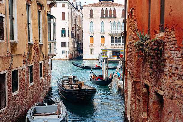 Boats are docked in a narrow canal surrounded by tall buildings in Venice.
