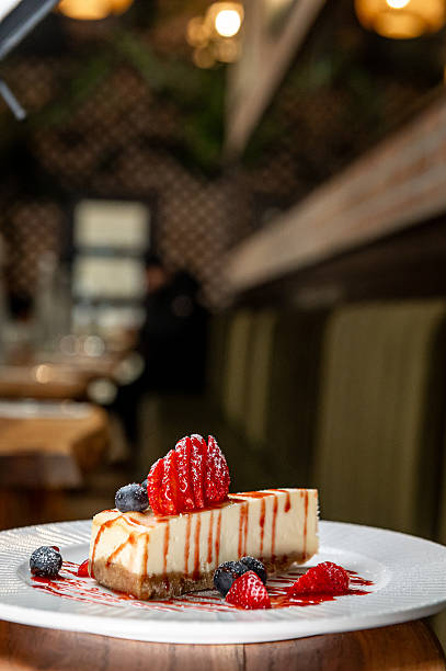 Dessert sits on a plate in a restaurant. A piece of cheesecake topped with berries rests on a white plate in a restaurant during dinner time.