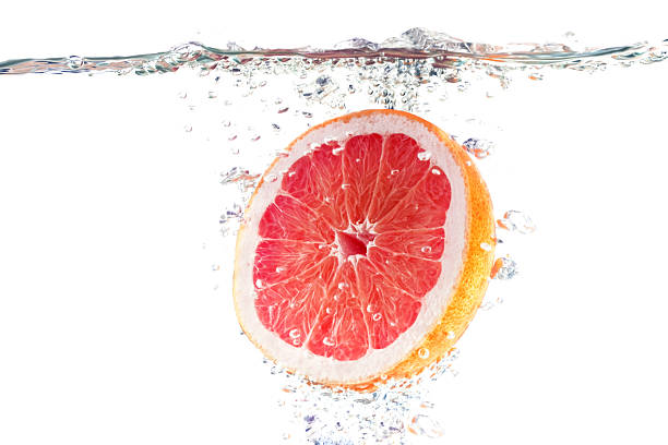 Grapefruit Slice Underwater with Bubbles and Visible Water Surface on White Background