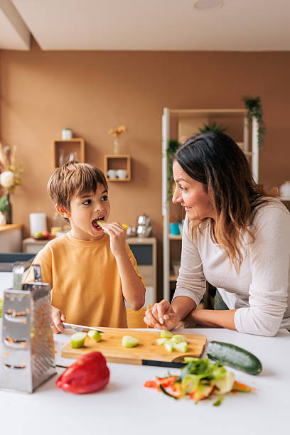 Young Boy Tasting Fresh Cucumber While Cooking With Mother