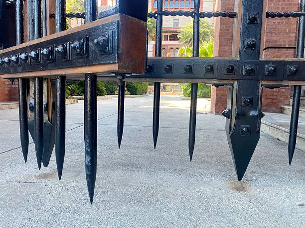 Detailed close-up of sharp iron gate spikes with historic brick building in the background. Architectural detail with strong perspective and texture.