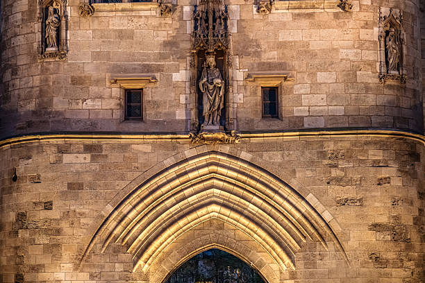 Night view of a historic stone city gate in Bordeaux, France, featuring a carved statue above a lit Gothic archway, warm masonry tones and detailed architectural ornamentation in close-up.