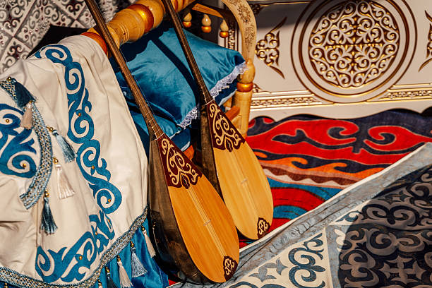 Two Decorated Dombra Lutes On Embroidered Textile And Colorful Carpet, Ornate Wooden Frame And Turquoise
