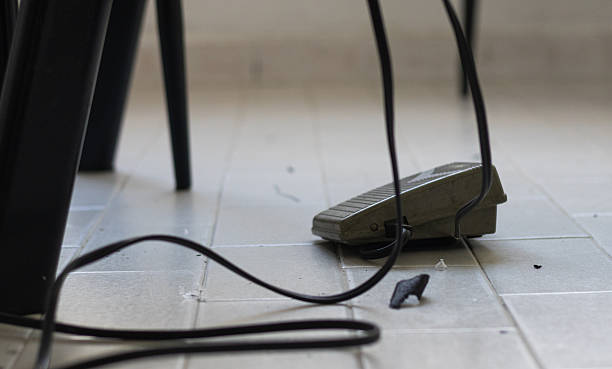 Sewing machine foot pedal with a tangled black cord resting on light gray tiled flooring, workshop environment, crafting
