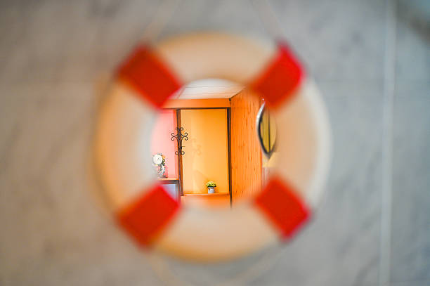 Lifebuoy with red stripes mirror hanging, showing  into interior room with warm light and maritime decor