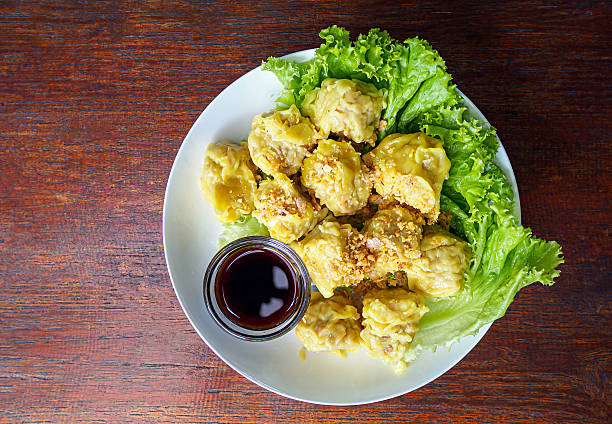 Thai steamed dumpling shumai with yellow sauce and dipping sauce on white plate, Rustic wooden table