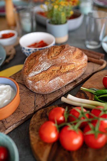 Close-Up of Homemade Bread with Cherry Tomatoes on the Table, Other Dishes are Blurred and visible Around