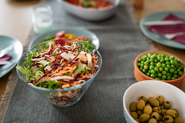 Salad, Peas and Olives on The Dining Table, with Plates and Other Food Blurred Around