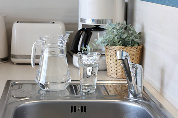 Clear water pitcher and glass on modern kitchen sink. Drinking water from kitchen faucet.