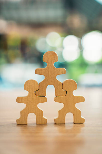 Wooden people figures stacked in a pyramid on a desk with blurred bokeh background. Concept of teamwork, business leadership, human resources, or family support. Corporate organization.