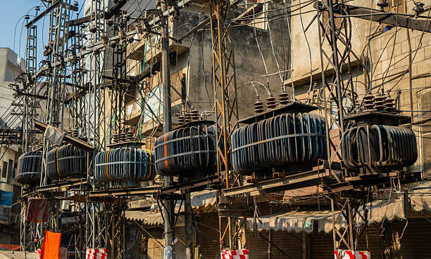 A complex web of power lines and heavy electrical transformers suspended above a street. An urban scene showing a highly disorganized, overloaded electrical distribution system in Lahore, Pakistan.