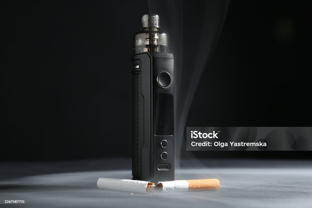 Electronic smoking device and broken cigarette in smoke on dark table against black background, closeup Addiction Stock Photo Electronic smoking device and broken cigarette in smoke on dark table against black background, closeup Addiction Stock Photo