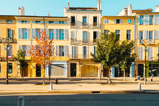 Row of pastel ochre and yellow buildings lining a tree-lined boulevard in morning light, with an autumnal plane tree, Aix-en-Provence, Provence, France.