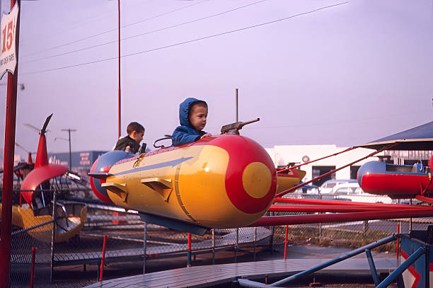 Color vintage photograph of a young child riding a small airplane themed amusement ride at a carnival or amusement park in 1965