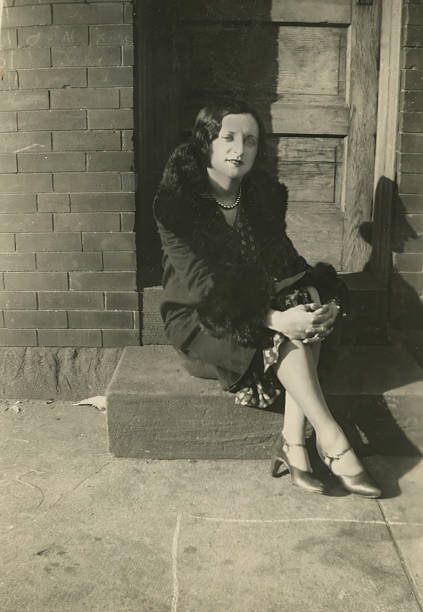 Young woman in 1920s clothing sits on a step in front of a door on a sidewalk in Philadelphia 1928.