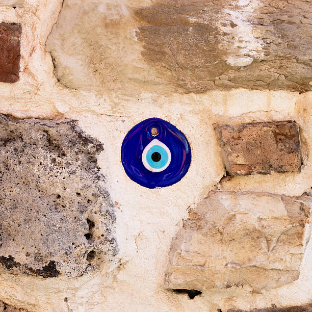 Close-up of a blue glass evil eye bead (Nazar Boncuğu) embedded in an old natural stone wall, traditional Turkish amulet for protection against the evil eye on a rustic masonry surface.