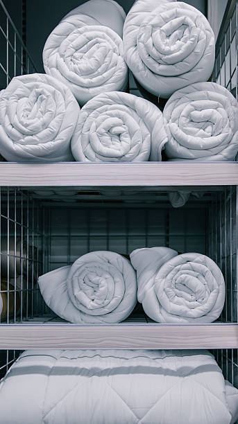 A retail display showcasing rolled bedding items, including duvets and comforters, organized on shelving units for sale