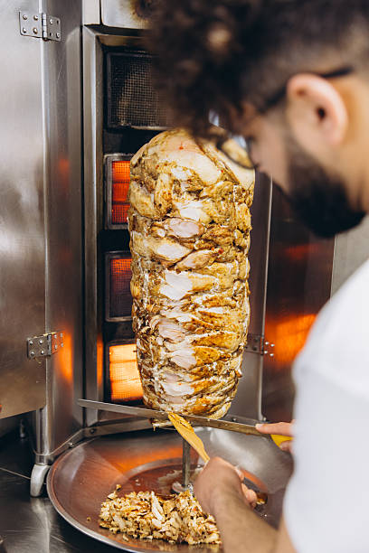 Arab man preparing shawarma, slicing grilled chicken from a rotating vertical spit for Middle Eastern street food