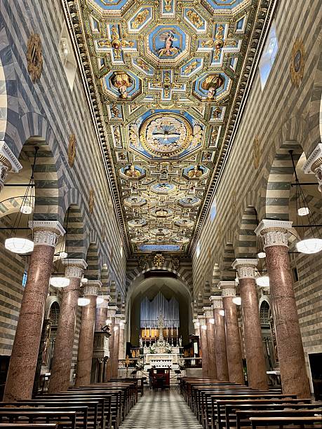 Volterra Cathedral featuring an ornate Renaissance ceiling, long nave with striped walls, marble columns, and empty pews leading to the impressive altar and pipe organ in Italy