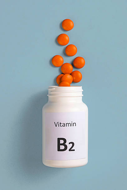 White plastic bottle with Vitamin B2 (Riboflavin) tablets on a blue surface, representing energy production, and supports healthy skin and eyes