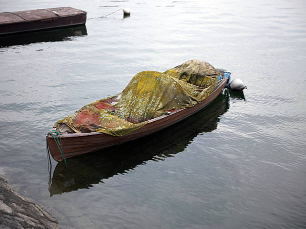 Small wooden boat covered with a weathered tarp floating on calm lake water, evoking stillness, time passing and quiet lakeside atmosphere.