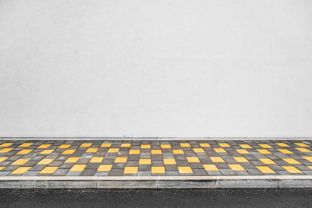 Patterned pedestrian pavement beside blank white facade, minimalist city street scene.