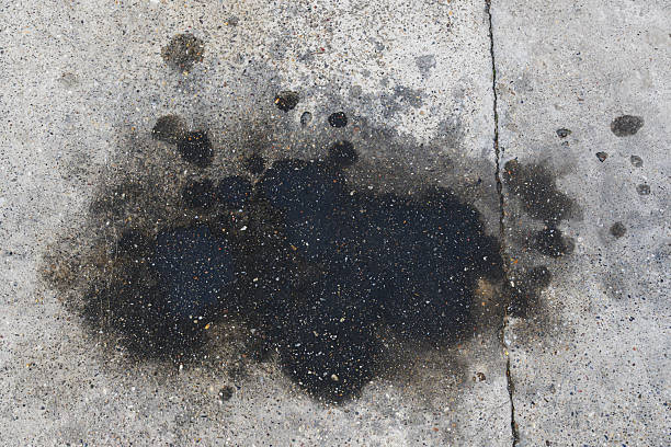 Dark iridescent oil stain puddle on weathered gray concrete sidewalk.