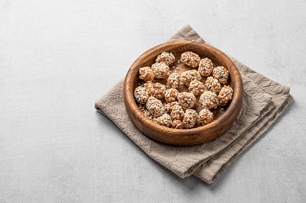 Sugar-coated peanuts with sesame seeds in a wooden bowl on a linen napkin