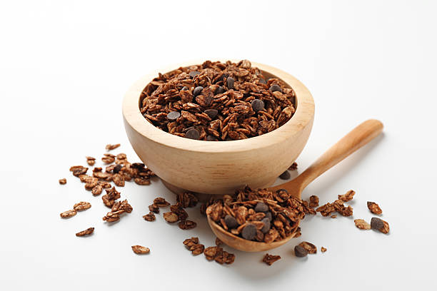 Delicious granola with chocolate chips in bowl and spoon on white background, closeup