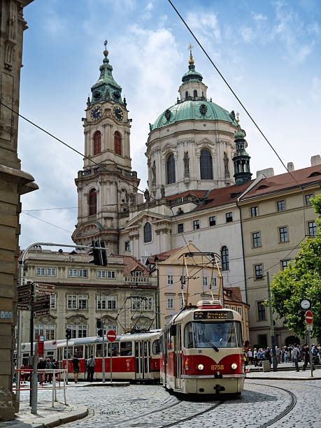 Red And White Tram Passing Through Busy Historic Square With Majestic Saint Nicholas Church Bell Tower And Dome In Background, Prague, Czech Republic