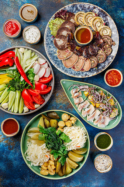 Bowls with different foods including various meat snacks, vegetable snacks made from fresh and fermented vegetables and sauces. A table with many bowls of food on it.