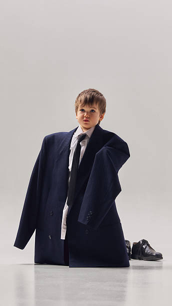 Little boy wearing oversized business suit standing in studio with large jacket and tie. Concept of future career dreams, leadership ambition and childhood imagination.