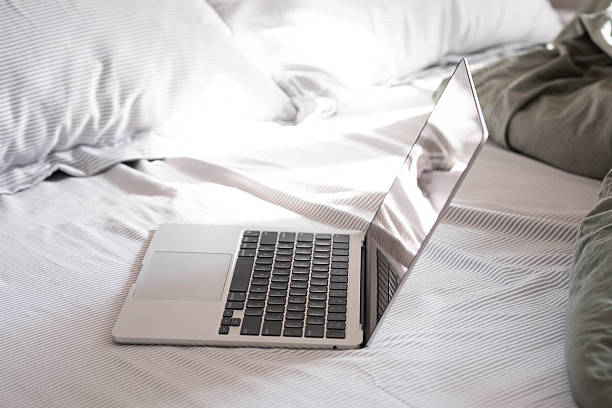 A silver laptop lies open on a pristine white bed, inviting a moment of work or leisure in comfort.