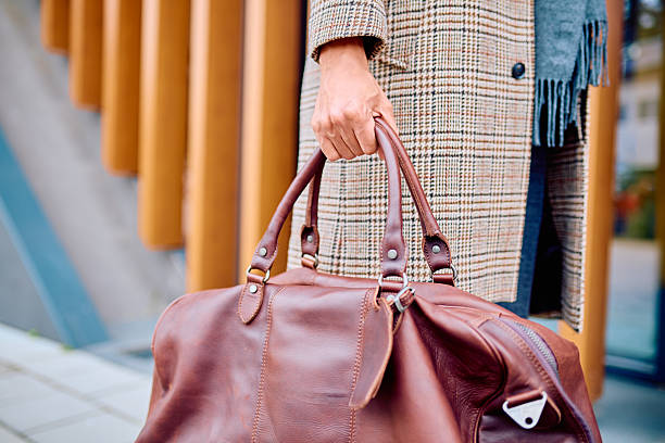 Adult person holding a stylish brown leather duffel bag. Preparing for travel, a business trip, or a weekend getaway