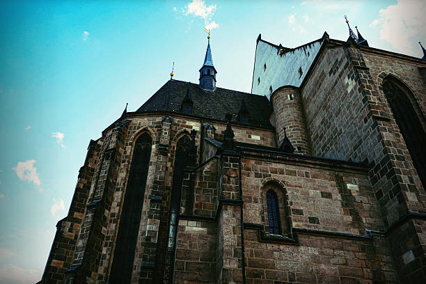 Detailed low-angle view of a massive historical gothic cathedral with stone walls, tall arched windows, and towers against a clear blue sky