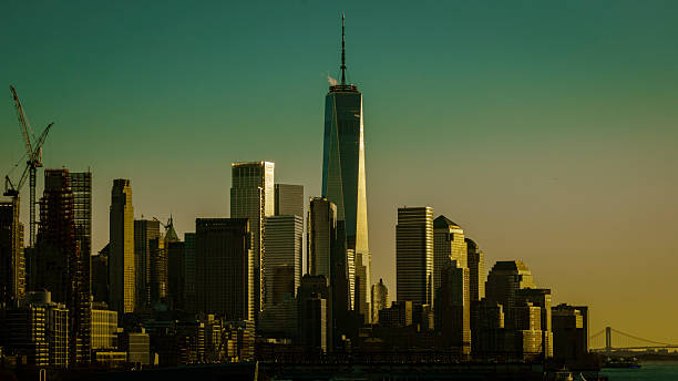 Golden hour view of the New York City skyline featuring One World Trade Center illuminated by warm sunlight, capturing the modern architecture of Lower Manhattan.