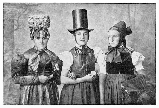 Authentic 19th-century black and white studio portrait of three young women wearing elaborate and distinct traditional German folk costumes (Tracht). The woman in the center wears a top hat, the woman on the left a 'Schäppel' festive crown, and the woman on the right a bonnet. This photograph documents the rich cultural heritage and diversity of regional dress in 19th-century Europe. Halftone print from a publication.