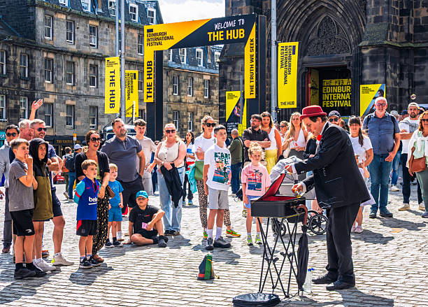 Edinburgh, Scotland - An audience watching as a street artist performs magic tricks outside the Edinburgh International Festival Hub on the Royal Mile.